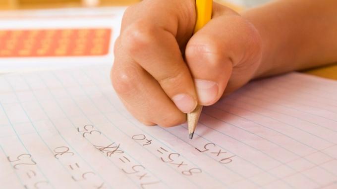 La mano di un bambino che completa un compito a casa con l'aiuto di sistemazioni matematiche